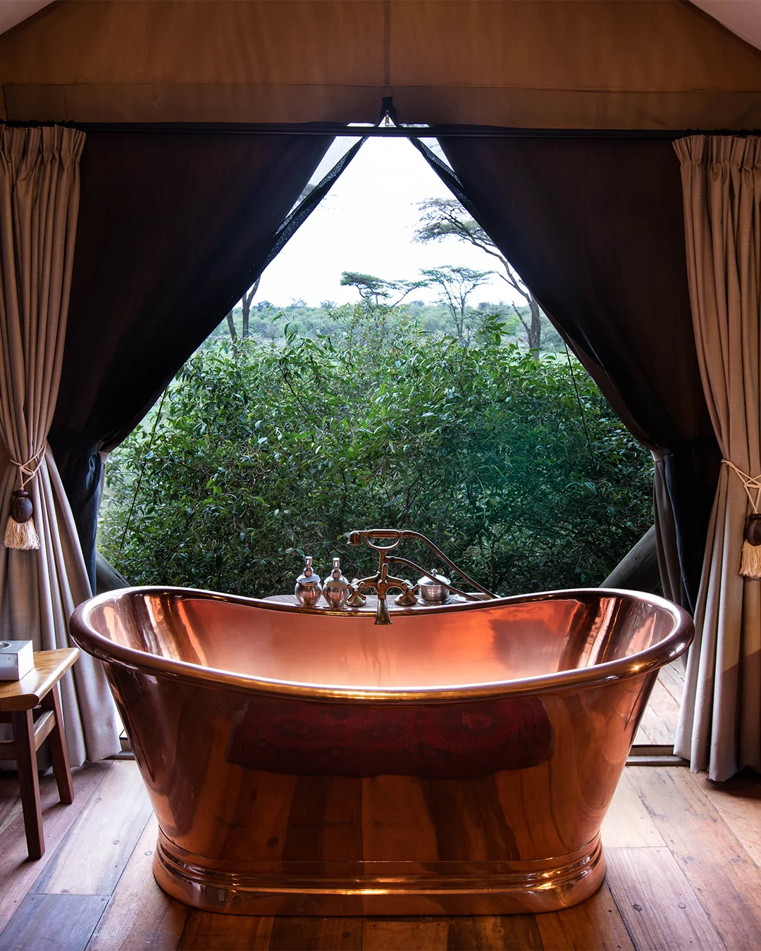A copper bath opening towards trees through tent curtains
